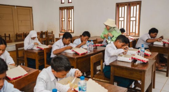Siswa sekolah menengah di Kawasi menikmati makanan bergizi gratis di dalam ruang kelas sebagai bagian dari program pemenuhan gizi Harita Nickel.