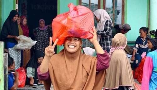 Seorang ibu rumah tangga tersenyum lebar sambil mengangkat paket sembako di atas kepala saat bazar murah Ramadan di Desa Soligi.
