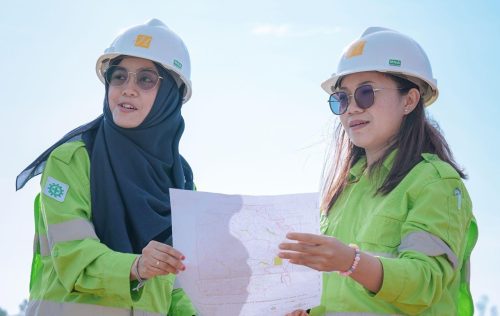 Dua pekerja perempuan mengenakan helm proyek dan seragam hijau berdiskusi sambil memegang peta di area operasional tambang Pulau Obi.